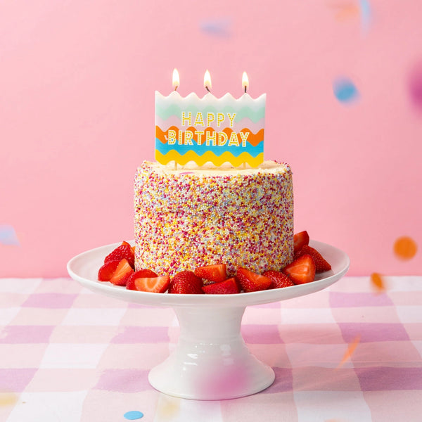 Colorful birthday cake with sprinkles and strawberries on a white cake stand against a pink background. wavy statement big block birthday candle unique fun cute adorable pickup or delivery Pittsburgh